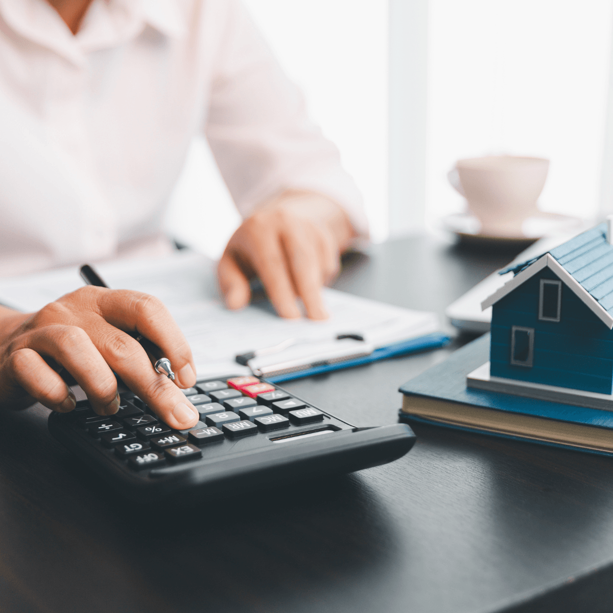 Person calculating mortgage figures with a calculator beside a small blue model home.