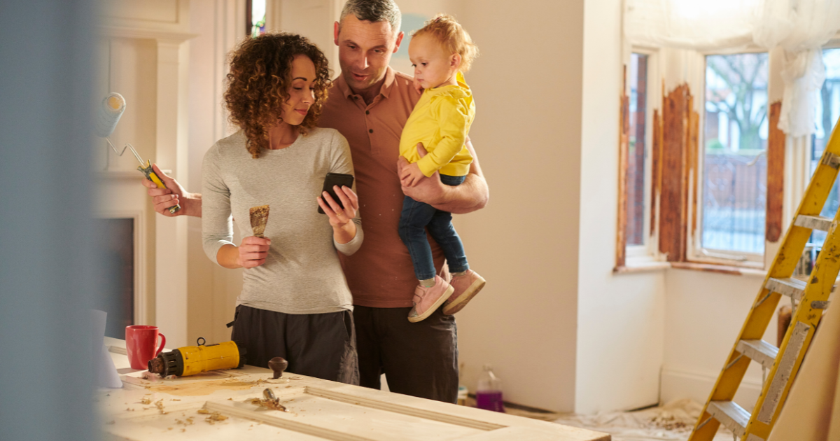 Couple renovating their home while checking renovation plans on a phone, with a young child