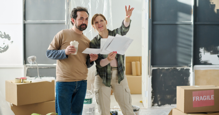 Couple reviewing renovation paperwork amid moving boxes during a phased home improvement project