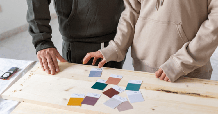 Two people comparing paint colour swatches laid out on a wood plank during a renovation