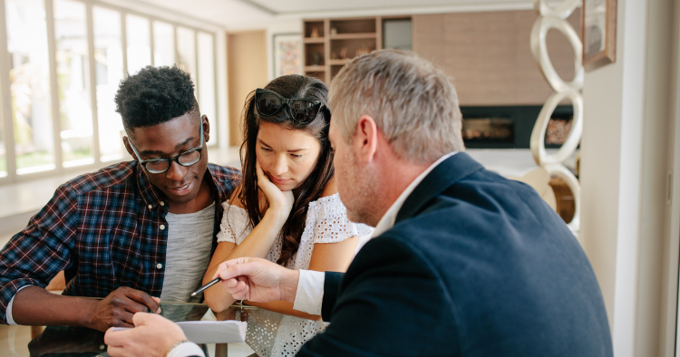 Couple sits with an advisor at a table while he reviews documents, the woman resting her chin on her hand